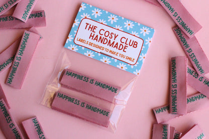Six handmade sewing labels with "Happiness is Handmade" text, designed for side seams, by The Cosy Club Handmade.