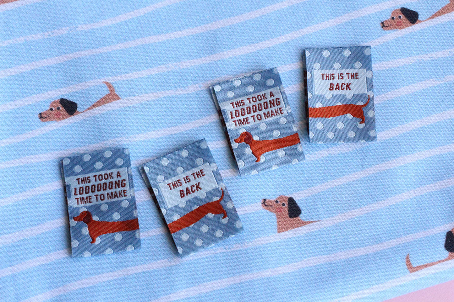 Blue sausage dog sewing labels by The Cosy Club Handmade, double-sided fabric tags with adorable dog design.