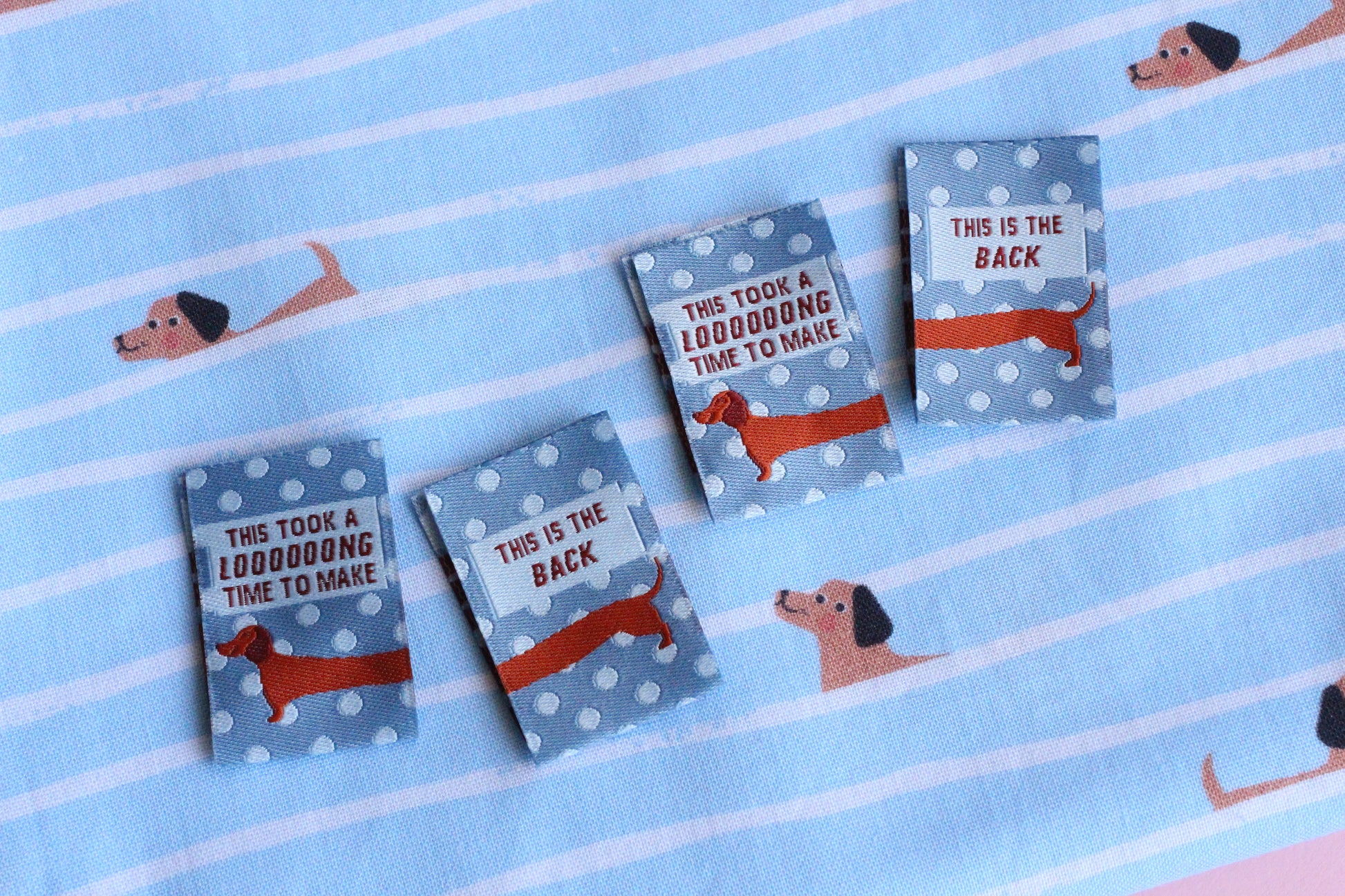 Blue sausage dog sewing labels by The Cosy Club Handmade, double-sided fabric tags with adorable dog design.