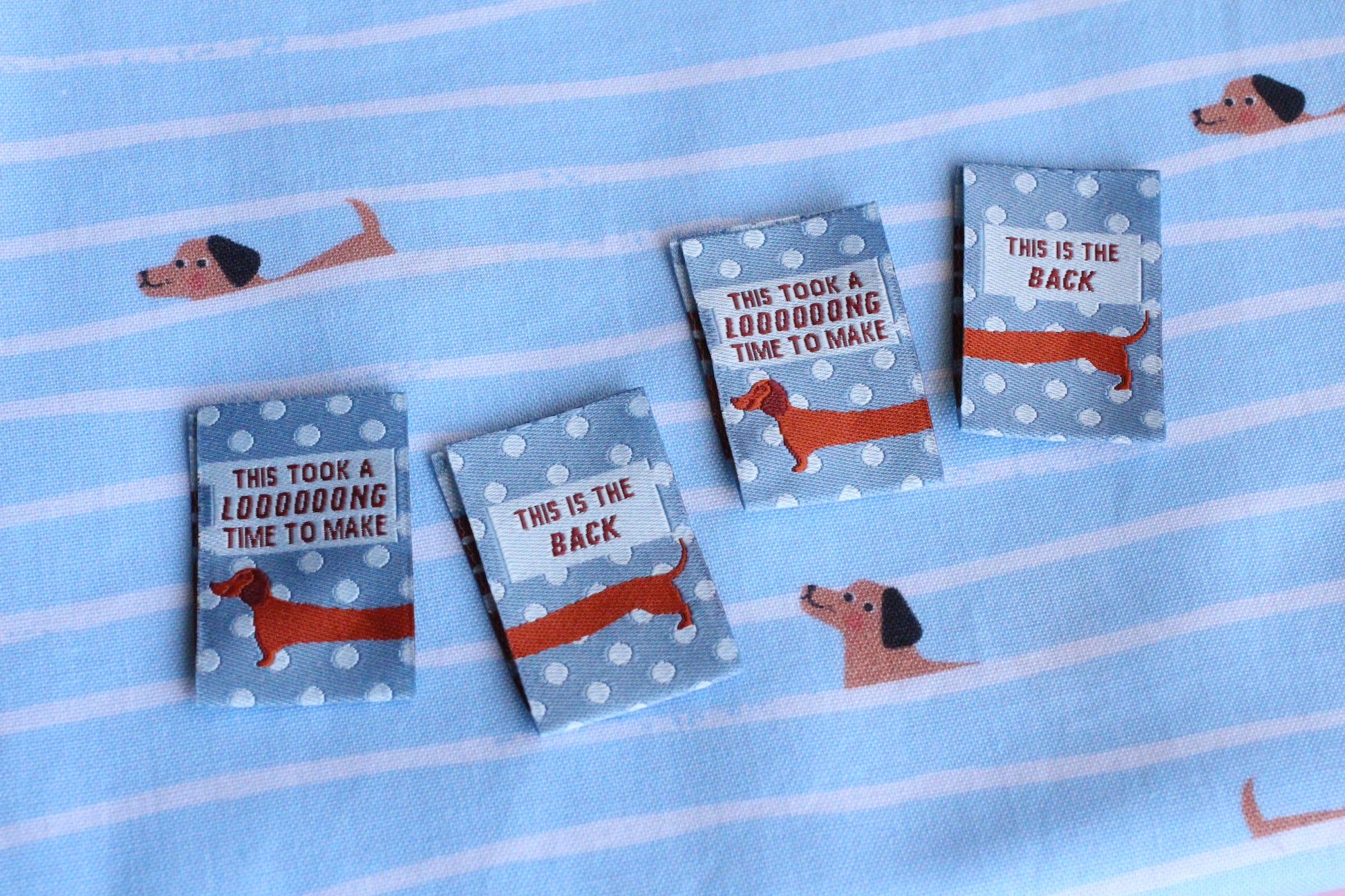 Blue sausage dog sewing labels by The Cosy Club Handmade, double-sided fabric tags with playful dog design for craft projects.