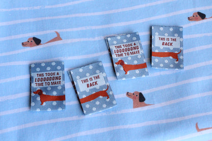 Blue sausage dog sewing labels by The Cosy Club Handmade, double-sided fabric tags with playful dog design for craft projects.