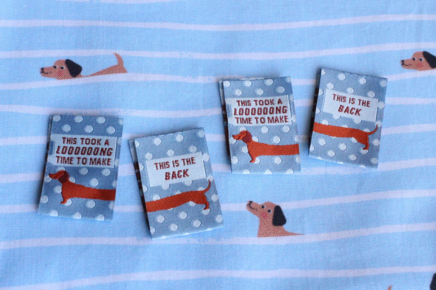 Blue sausage dog sewing labels by The Cosy Club Handmade, double-sided, perfect for crafting or sewing projects.