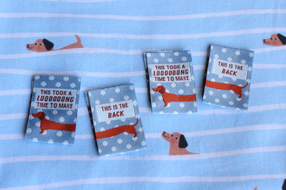 Blue sausage dog sewing labels by The Cosy Club Handmade, double-sided, perfect for crafting or sewing projects.