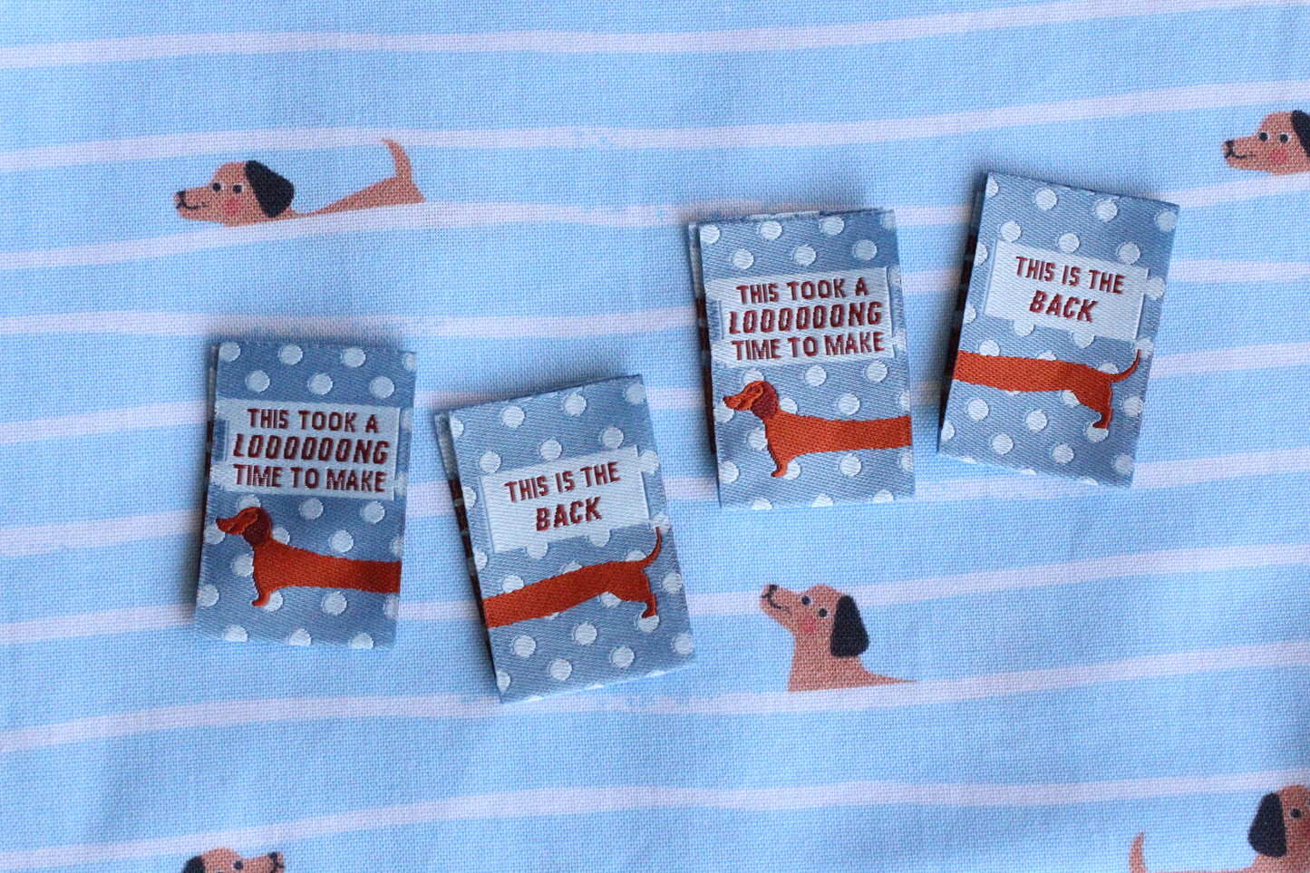 Blue sausage dog sewing labels by The Cosy Club Handmade, double-sided fabric tags with adorable dog design for craft projects.