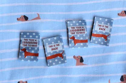 Blue sausage dog sewing labels by The Cosy Club Handmade, double-sided fabric tags with adorable dog design for craft projects.