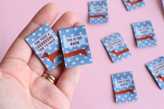 Blue sausage dog sewing labels from The Cosy Club Handmade, double-sided fabric tags with playful dog design for sewing projects.
