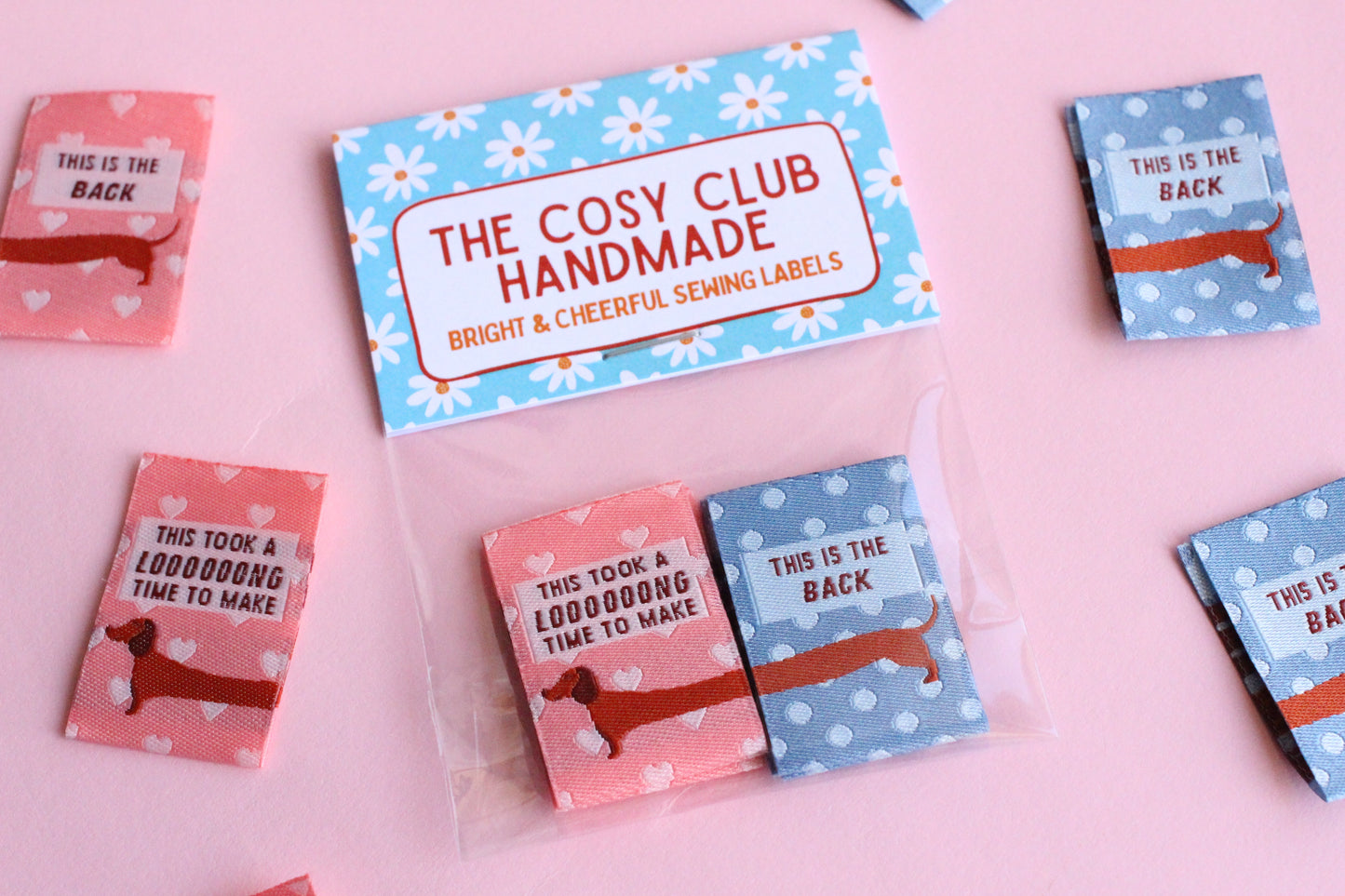 Pink and blue sausage dog sewing labels from The Cosy Club Handmade, double-sided fabric tags for clothing or craft projects.