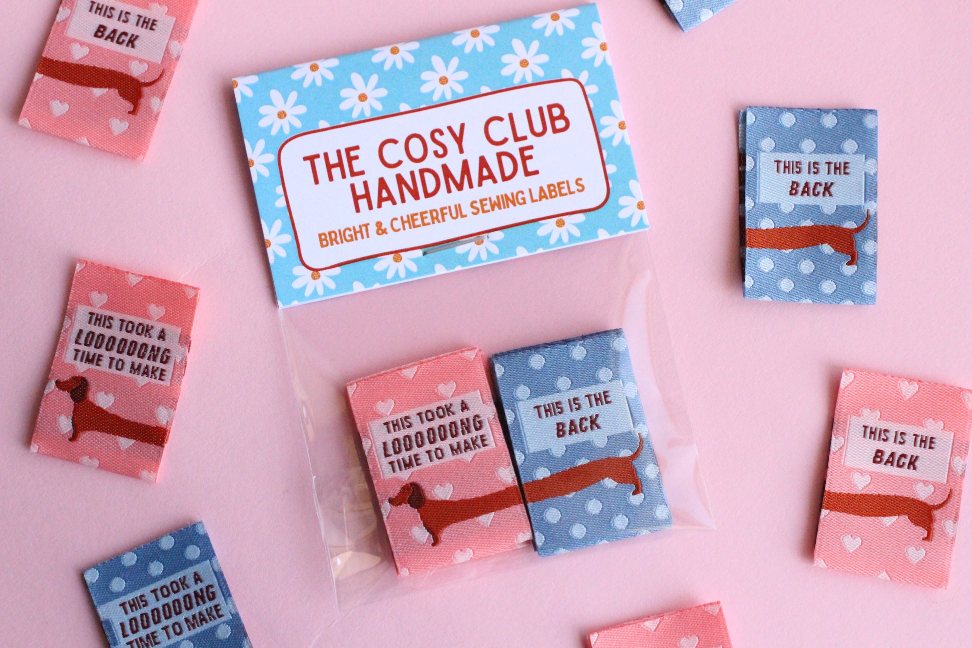 Pink and blue sausage dog sewing labels by The Cosy Club Handmade, double-sided fabric labels featuring cute dog designs.