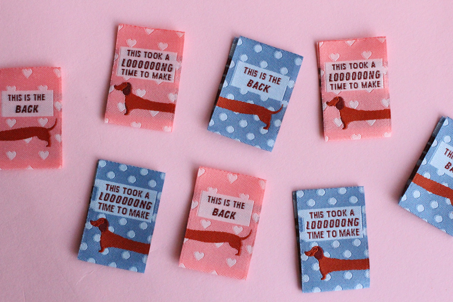Pink and blue sausage dog sewing labels from The Cosy Club Handmade, double-sided fabric tags for clothing or crafts.