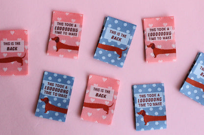 Pink and blue sausage dog sewing labels from The Cosy Club Handmade, double-sided fabric tags for clothing or crafts.