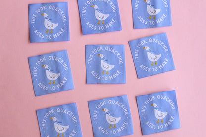 White goose sewing labels with "This Took Quacking Ages To Make" text from The Cosy Club Handmade, shown on a craft project.