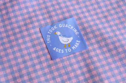 White goose sewing labels with "This Took Quacking Ages To Make" text by The Cosy Club Handmade, shown in close-up.