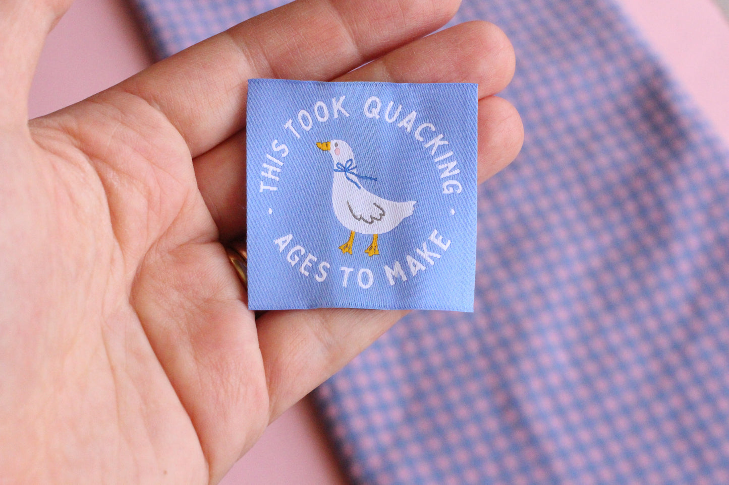 White goose sewing labels with "This Took Quacking Ages To Make" text from The Cosy Club Handmade, showing close-up of tags on fabric.