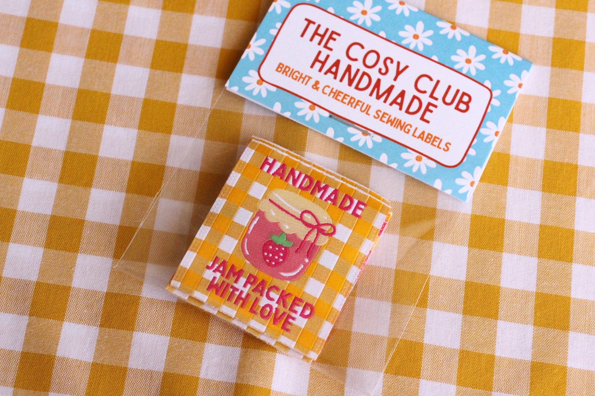Handmade sewing labels with "Jam Packed With Love" phrase by The Cosy Club Handmade, featuring colorful fabric and stitched edges.